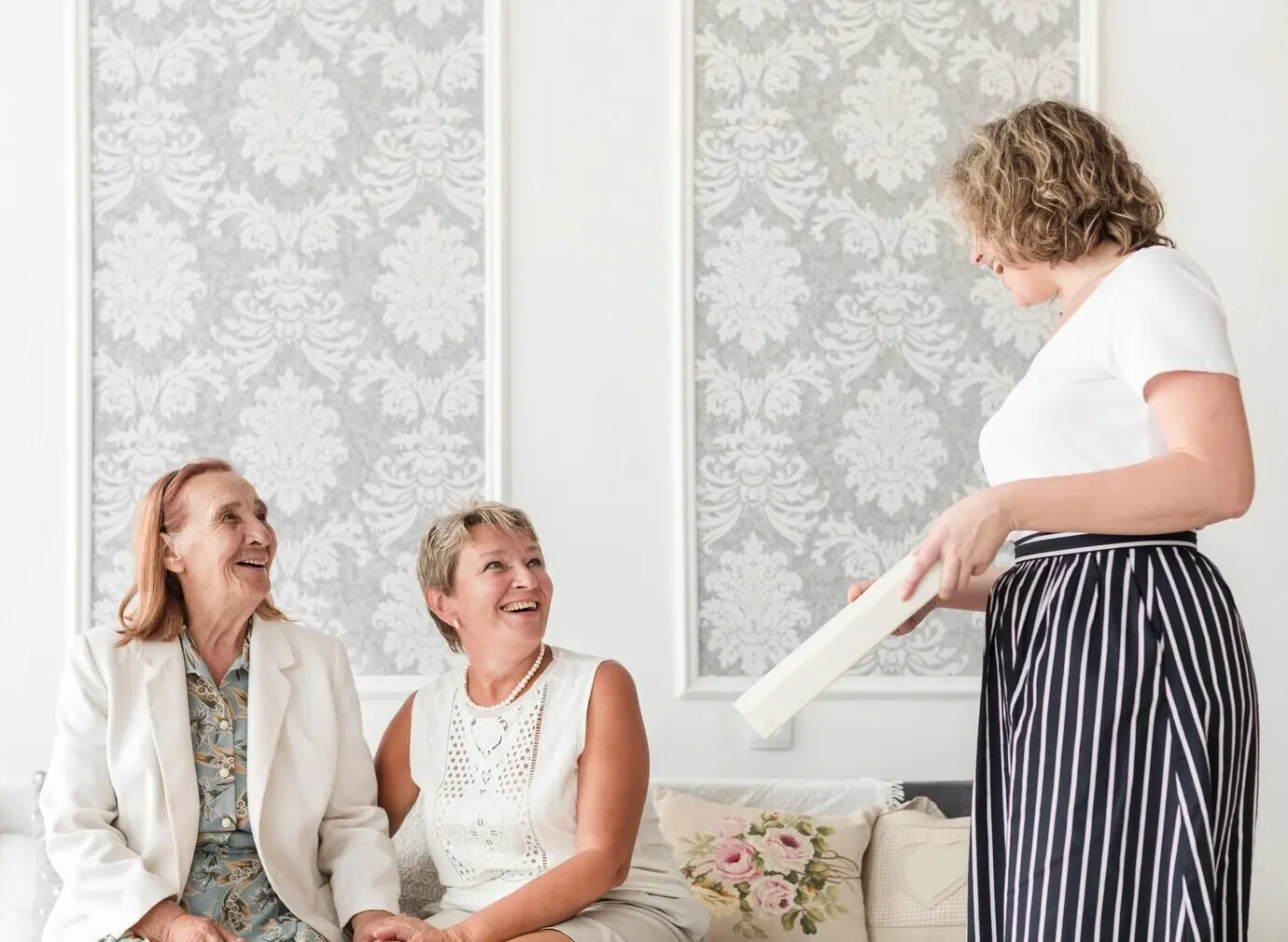 Mutter und Oma schauen ihre Tochter an, die zu Hause ein Fotoalbum hält.